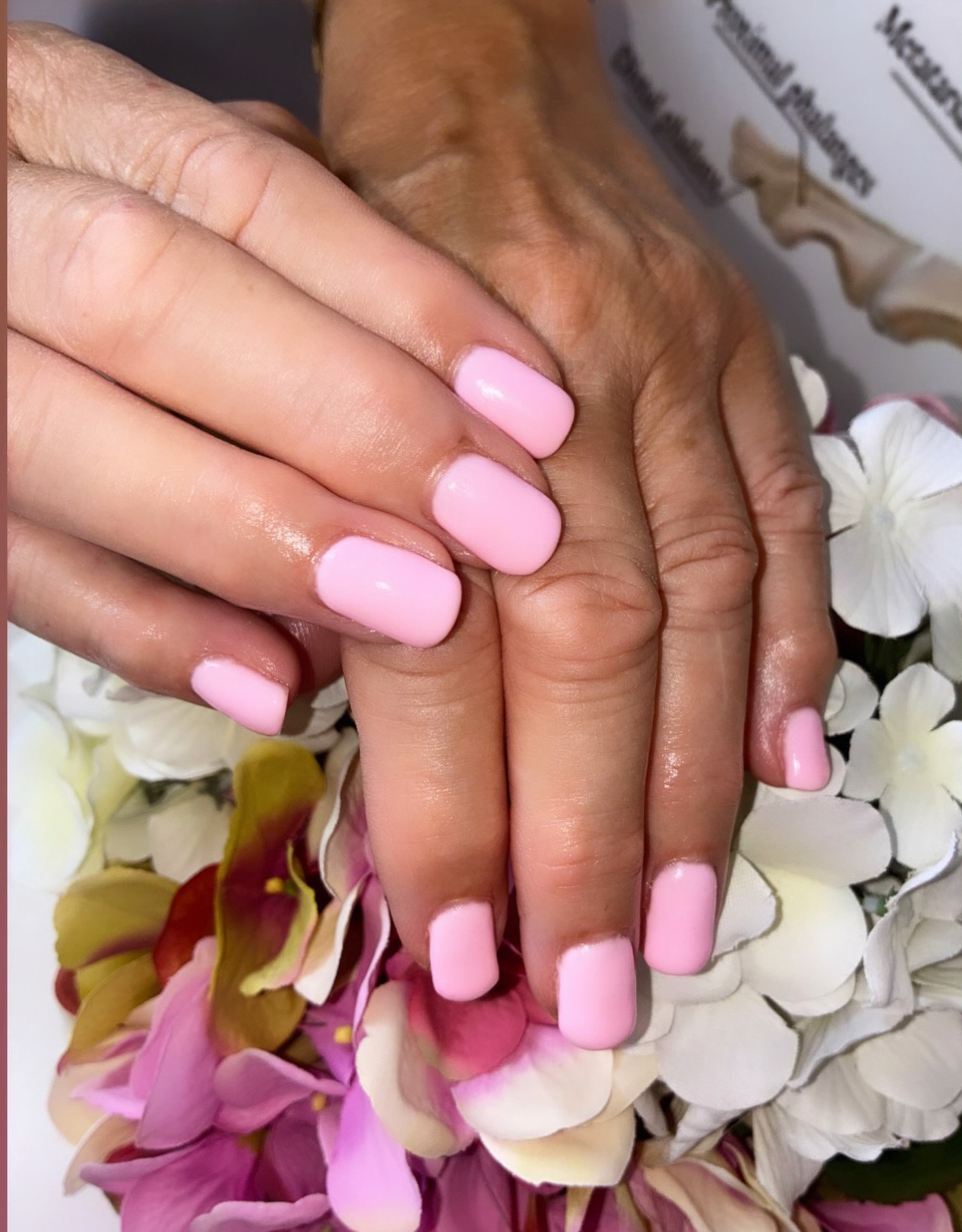 Twee handen met roze nagels boven bloemen